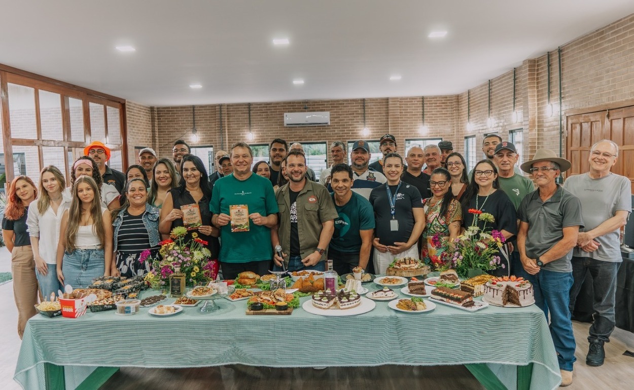 Participantes do Festival Sabores do Caparaó reunidos em torno de uma mesa com pratos típicos, doces e produtos da gastronomia regional em Ibitirama.