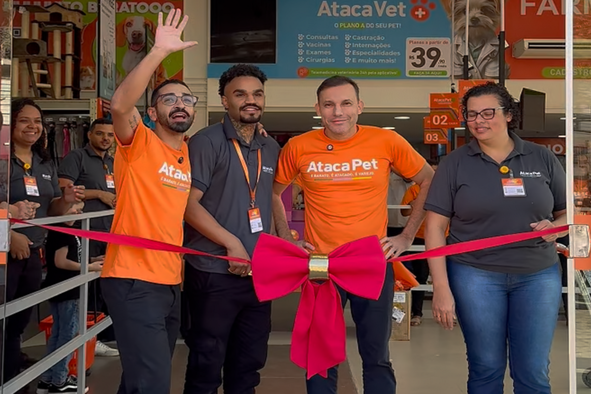 funcionários participam da inauguração de uma loja Ataca Pet, posicionados atrás de uma fita vermelha com um grande laço.