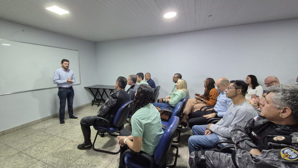 Homem apresenta informações a grupo sentado em sala de reunião, durante encontro sobre equoterapia com profissionais e policiais presentes.